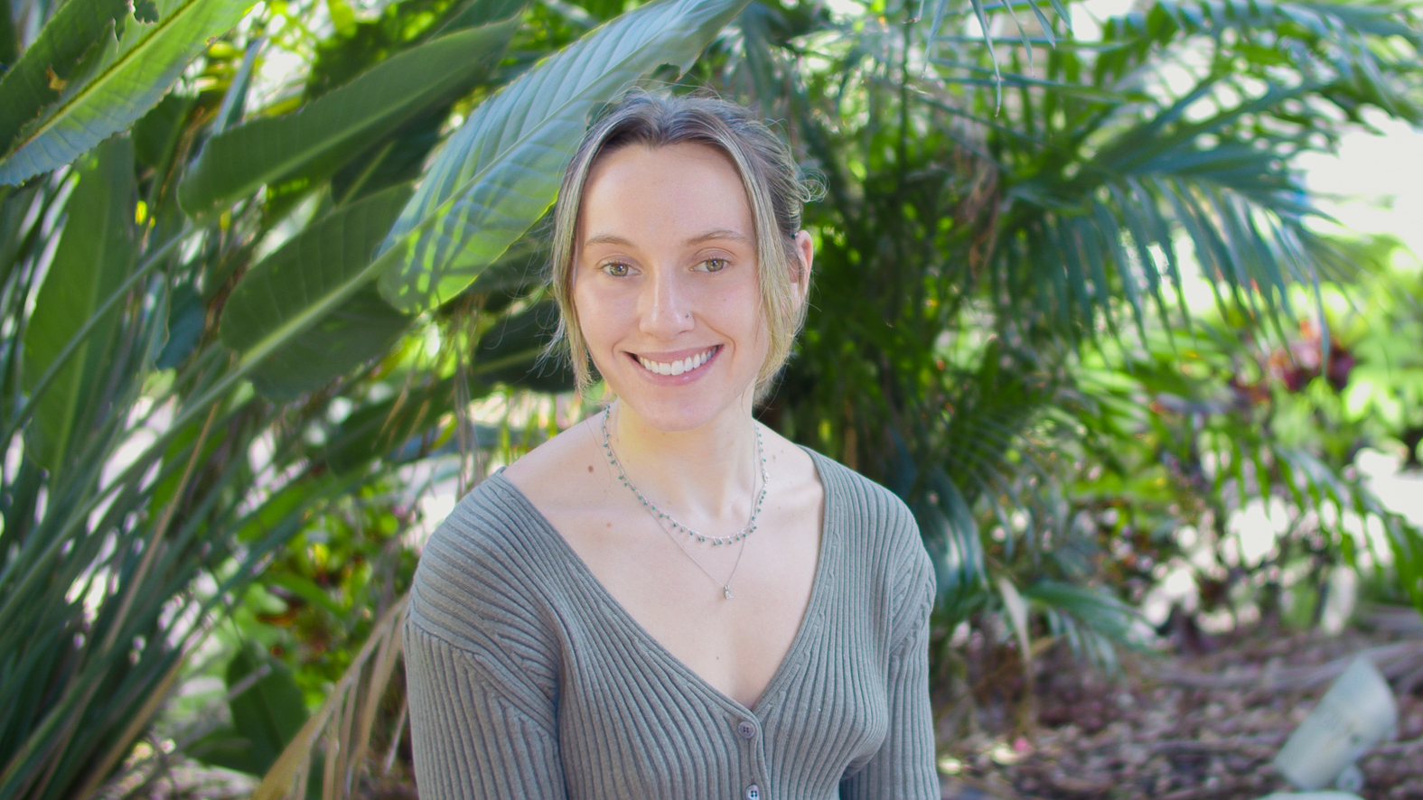 Lillian Reese, a white woman with brown hair and blonde highlights pulled back into a ponytail, smiling, 
                with brown hair, blonde highlights pulled back into a ponytail, wearing a green sweater. Lilly is in front of a blurred green background